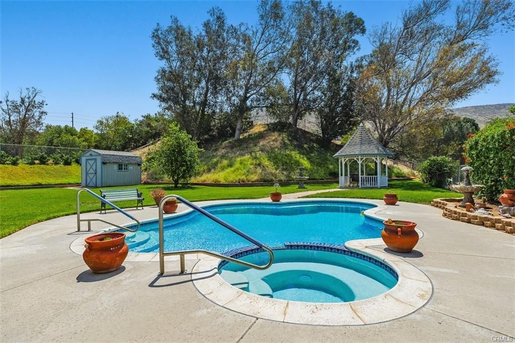 Backyard pool and spa with lounge area, potted plants, and gazebo under clear blue sky