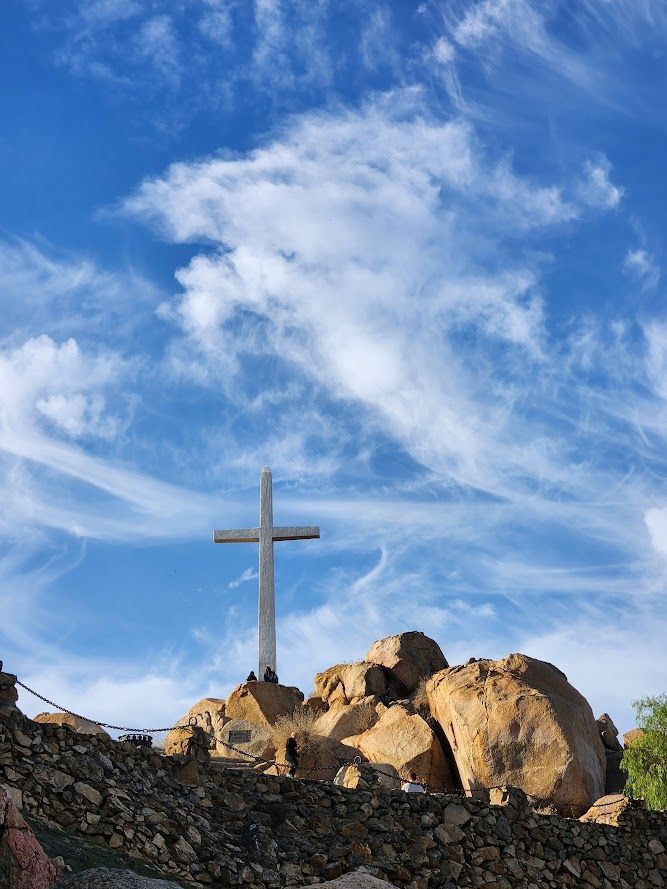 Cross on rocky hilltop under a blue sky with wispy clouds