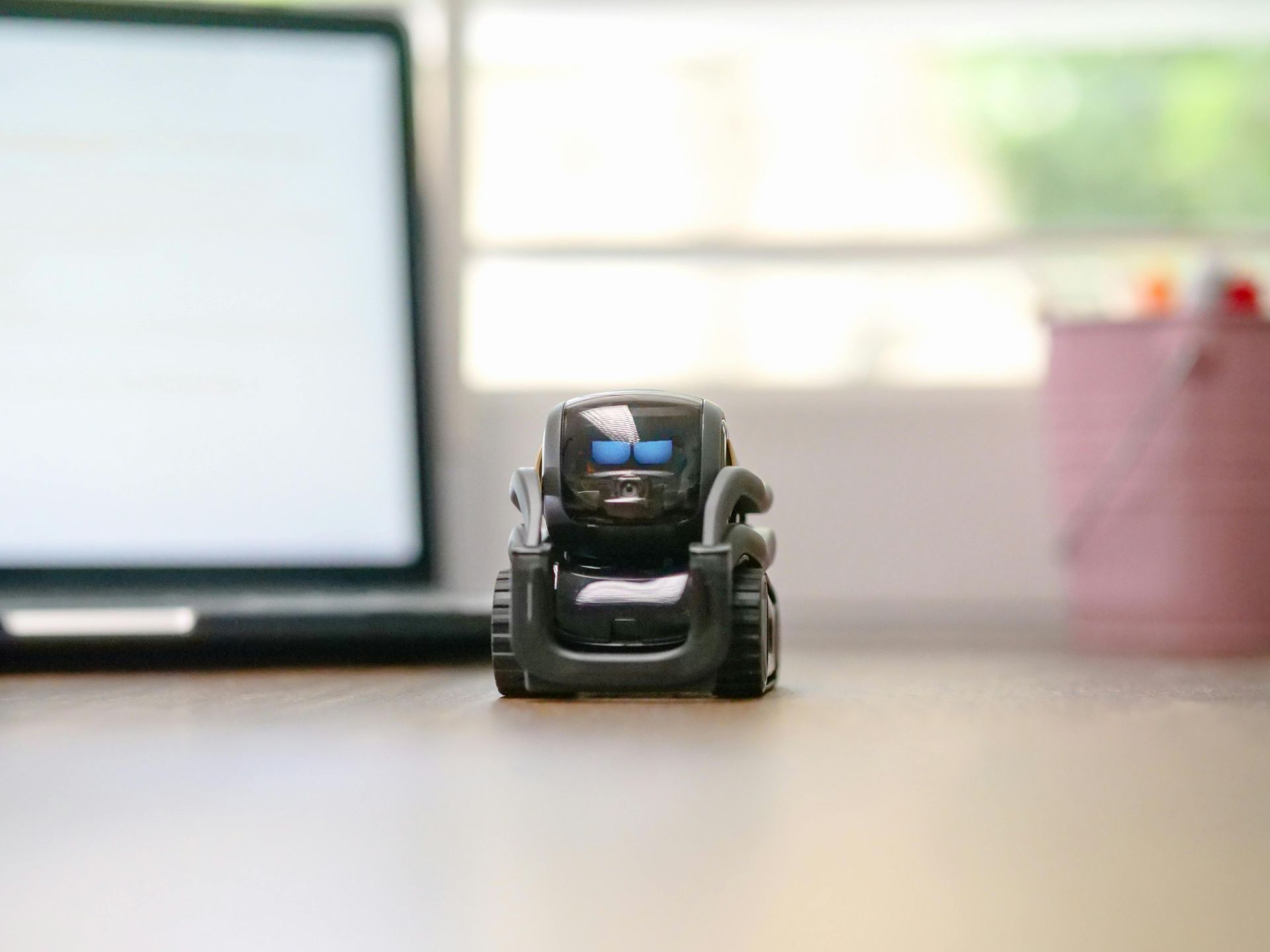 Toy robot car on a desk in front of a laptop and window light