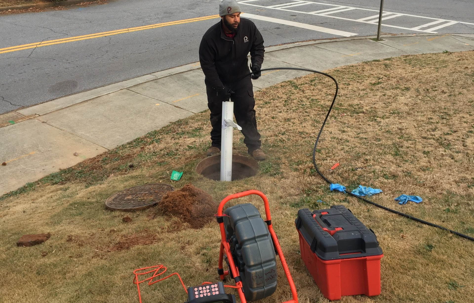 Man working on a well. He’s near a road, using equipment and tools on the ground.