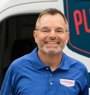 Man in blue polo shirt smiling, standing by a work truck with the Plumb Crazy logo.