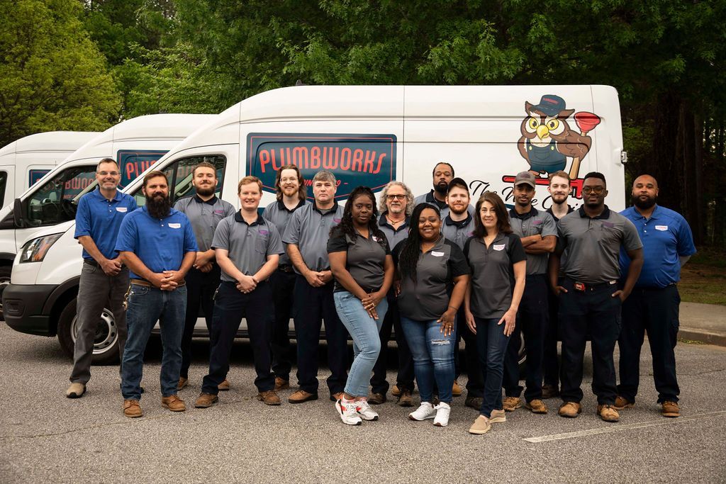The Plumbworks Team Plumbworks plumbing crew stands in front of vans; some wear blue, others gray shirts. Vans have logo on the side.