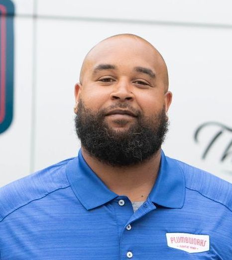 Man with dark beard wearing blue polo shirt, smiling in front of a white background with red and blue accents.