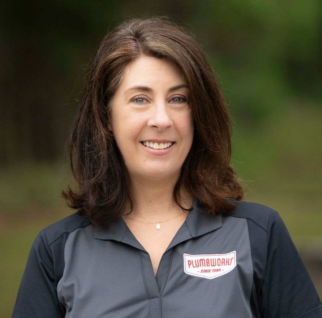 Woman in plumbing uniform smiles; logo on shirt.
