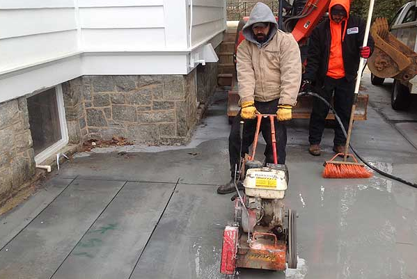 trenchless sewer pipe repair Man operating a concrete saw on a driveway. Another person nearby. Beside a house.