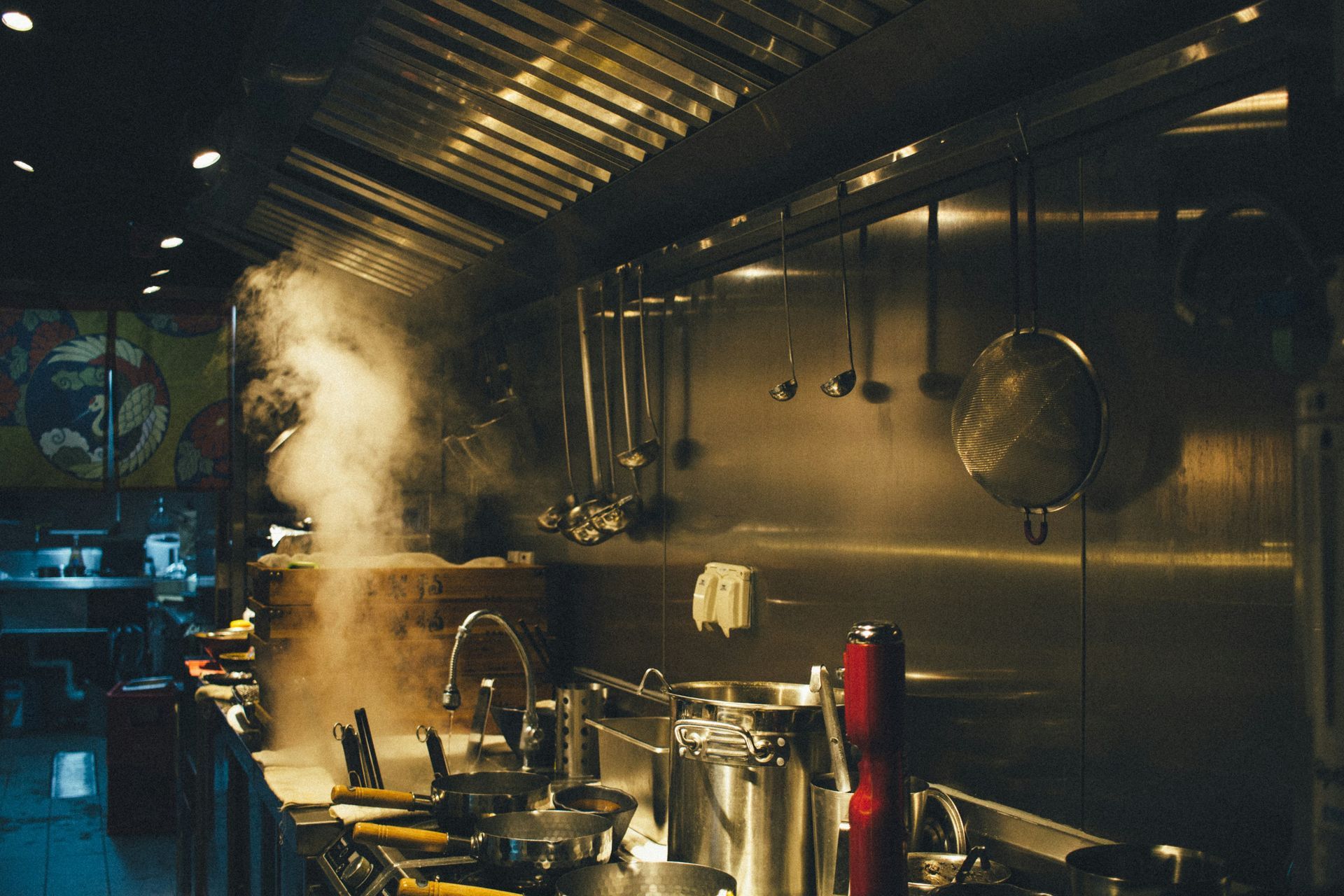 Steaming commercial kitchen with stainless steel surfaces and hanging utensils.
