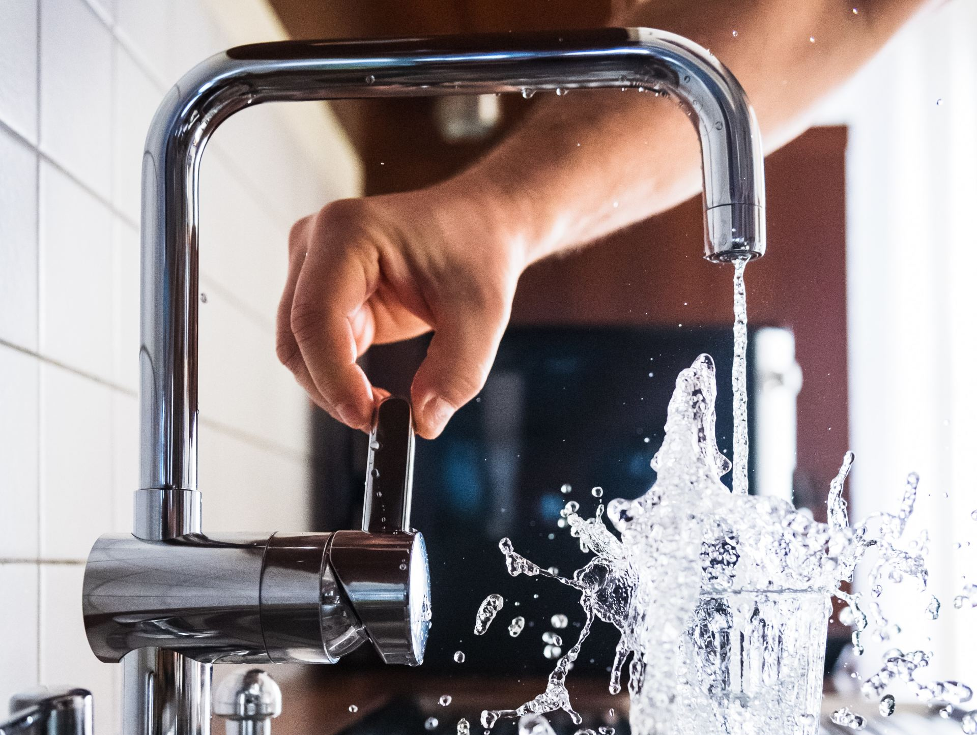Kitchen Plumbing A person turns on a chrome faucet, water splashing into a glass, kitchen setting.