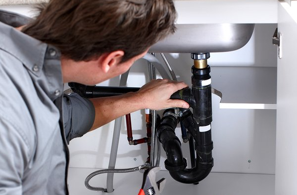 Leak Detection Plumber working under a kitchen sink, using a wrench to fix the pipes.