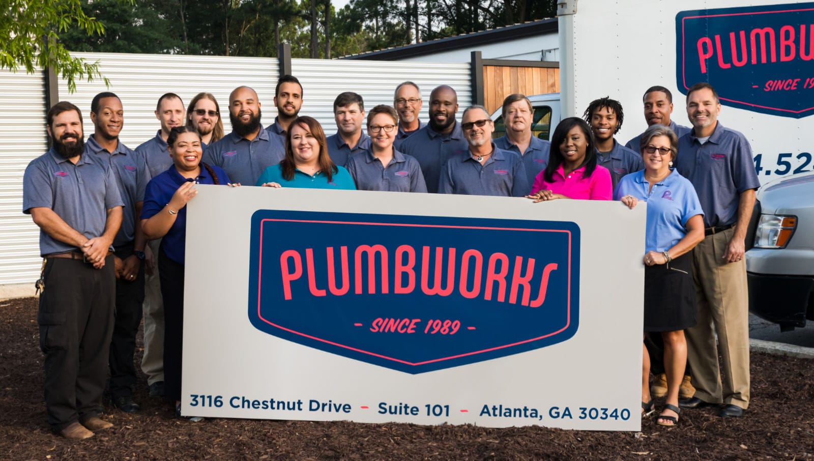 The Plumbworks Team Plumbworks staff, holding sign, pose outside a building in Atlanta, GA.