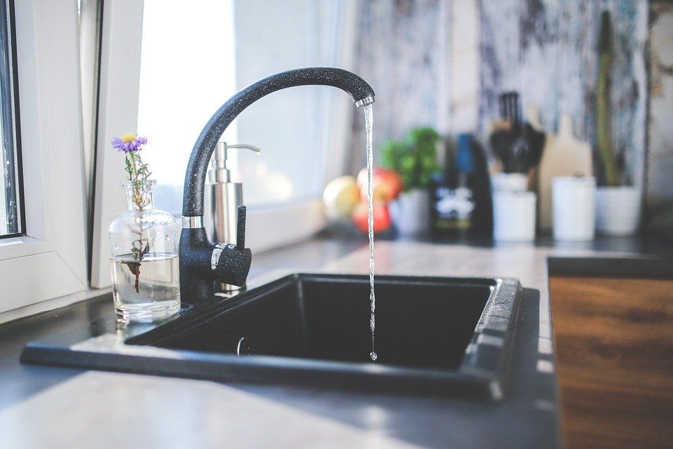 Water flowing from a black faucet into a black kitchen sink; a vase with a purple flower sits nearby.