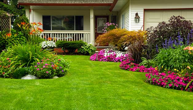 Atlanta Sewer Line Repair Well-manicured lawn and colorful flowerbeds in front of a white house with a porch and garage.