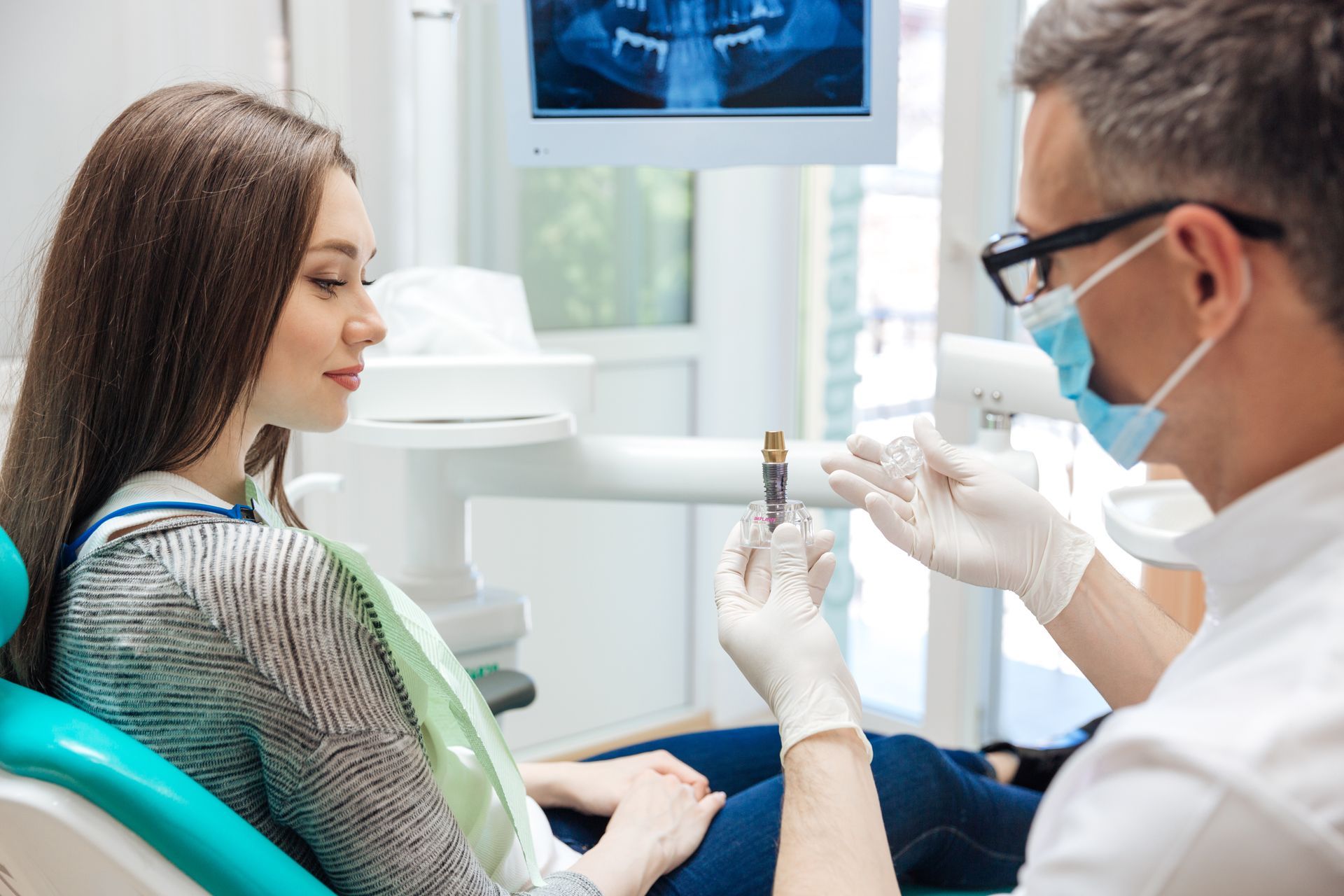 Dentist showing a dental mold to a seated patient in a bright clinic room