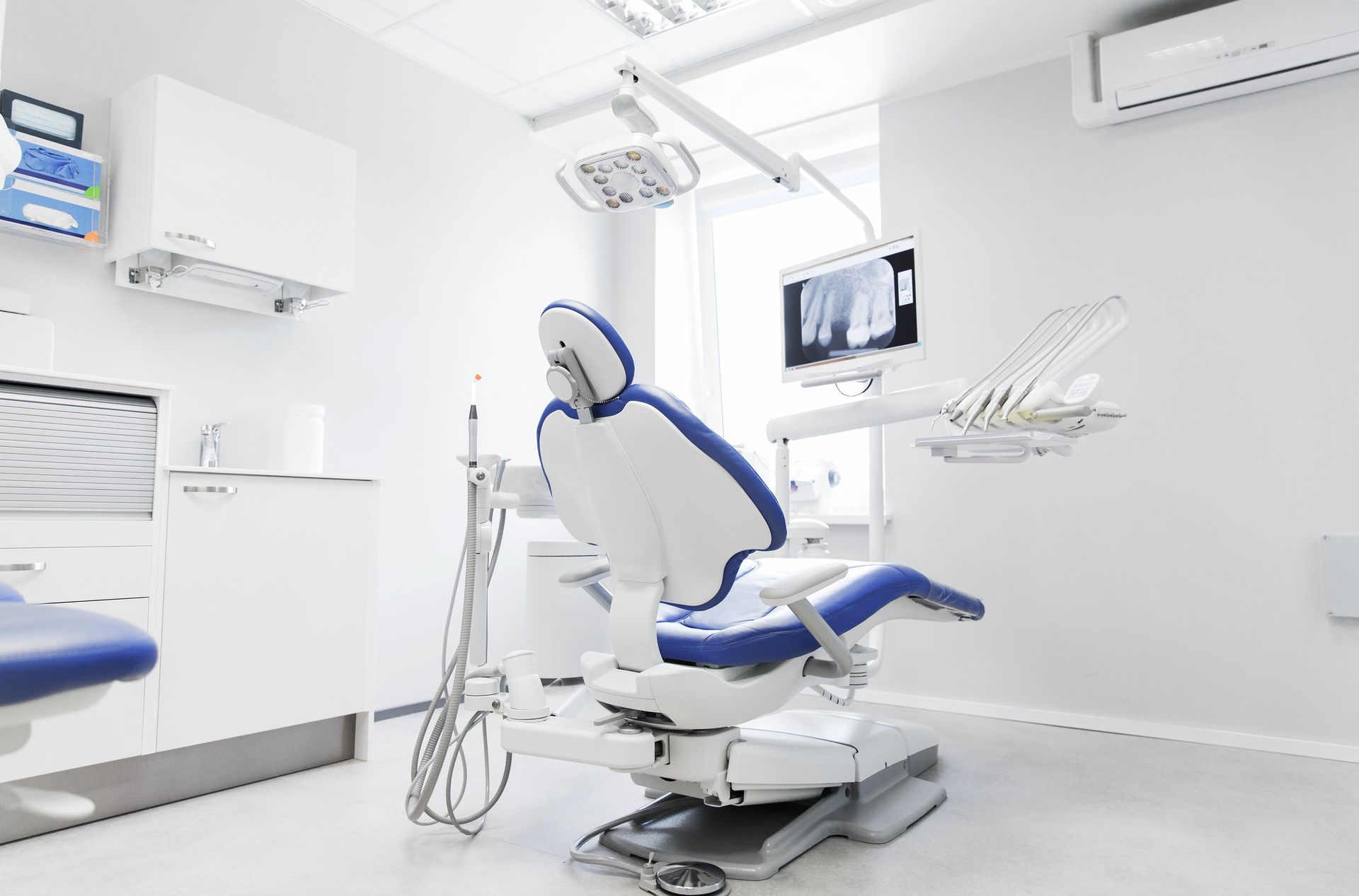 Bright modern dental exam room with a reclining chair, monitor, and wall-mounted equipment