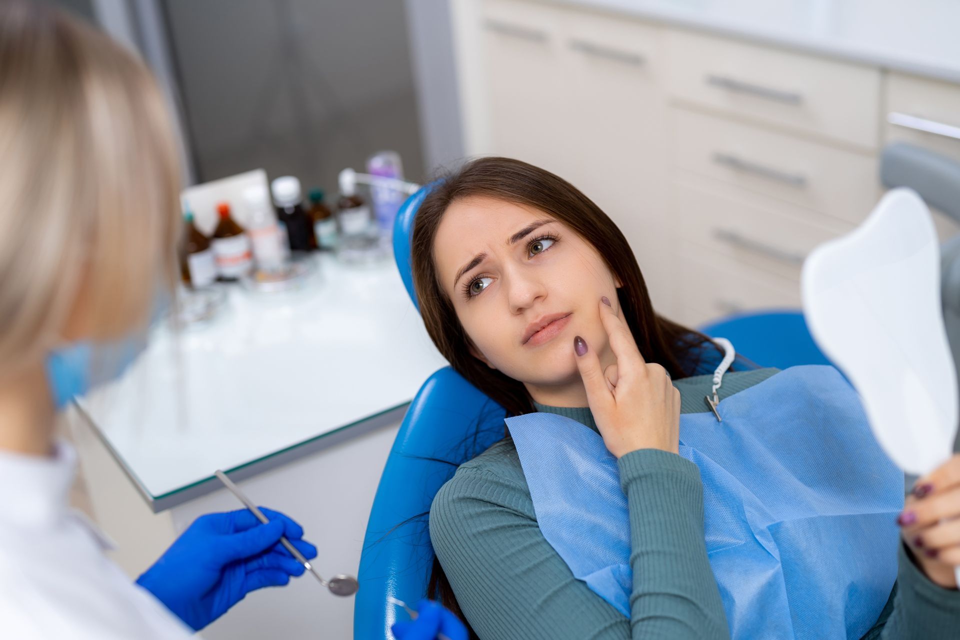 Dentist consulting a patient reclining in a blue dental chair, with tools nearby.