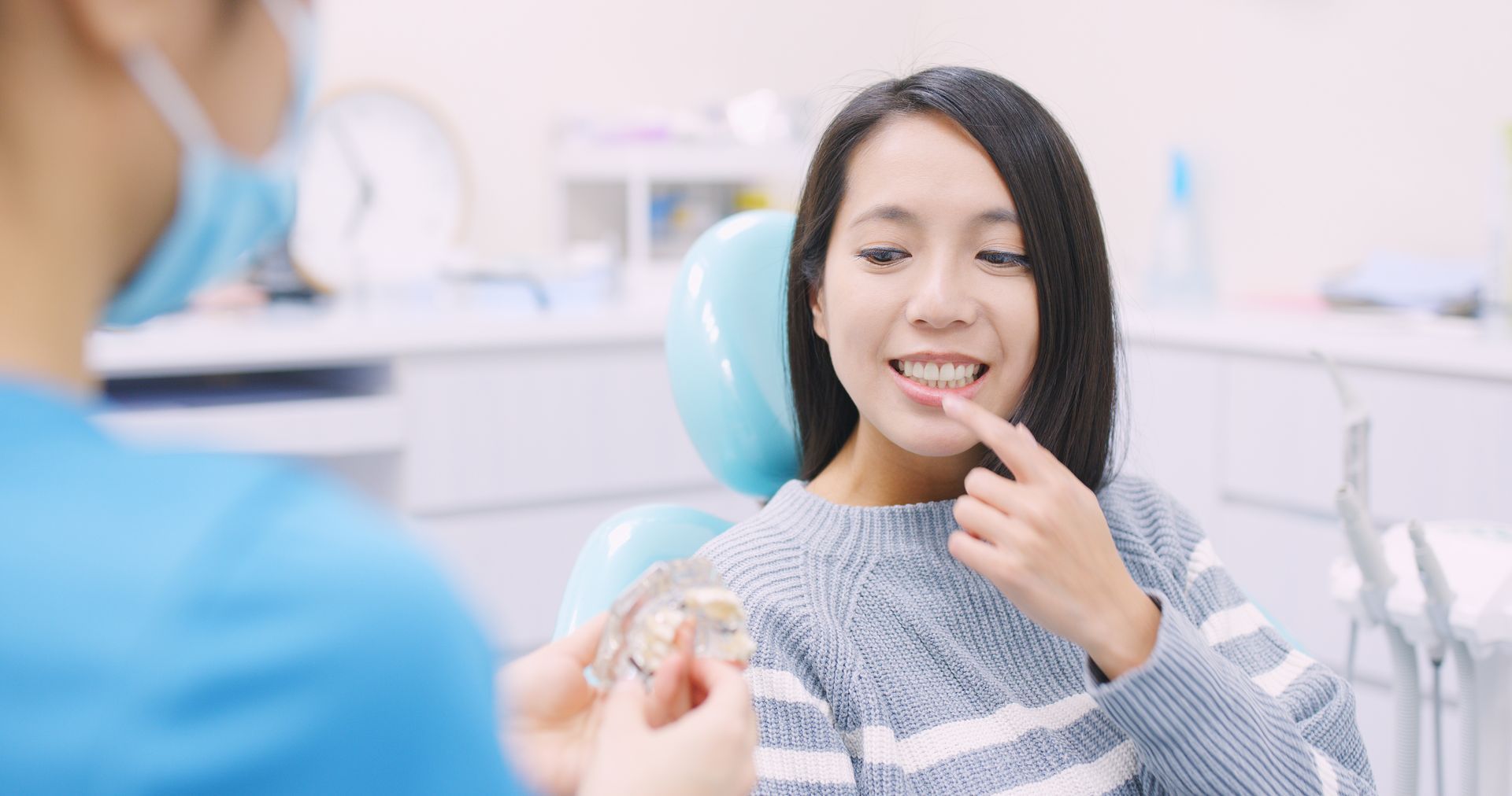 Patient smiling in a dental chair while a dentist shows a tooth model during an exam
