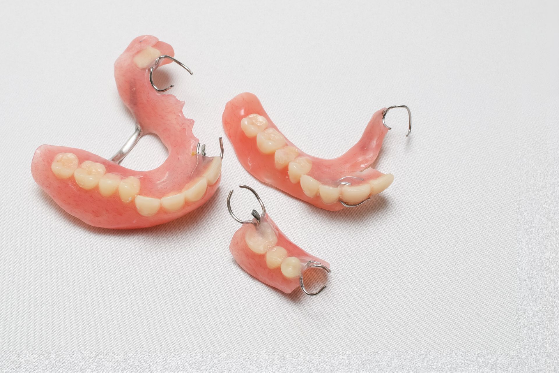 Broken pink dentures with metal clasps on a white surface