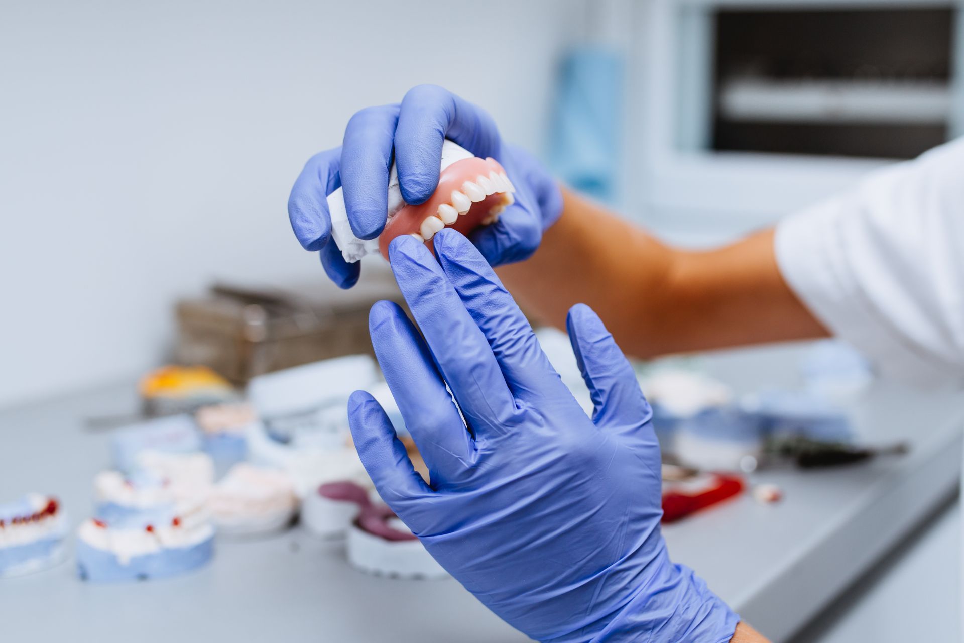 Blue-gloved hands adjusting a dental model on a workbench in a dental lab.