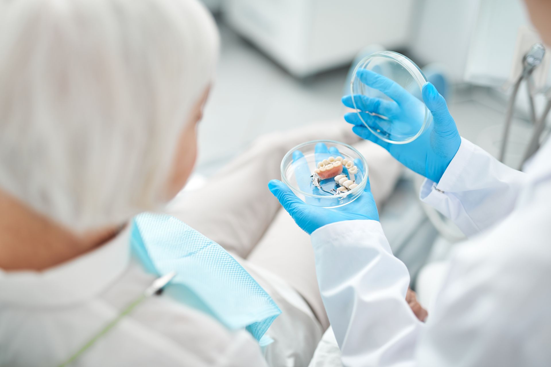 Healthcare worker in white coat and blue gloves examining a sample in a petri dish with a patient nearby