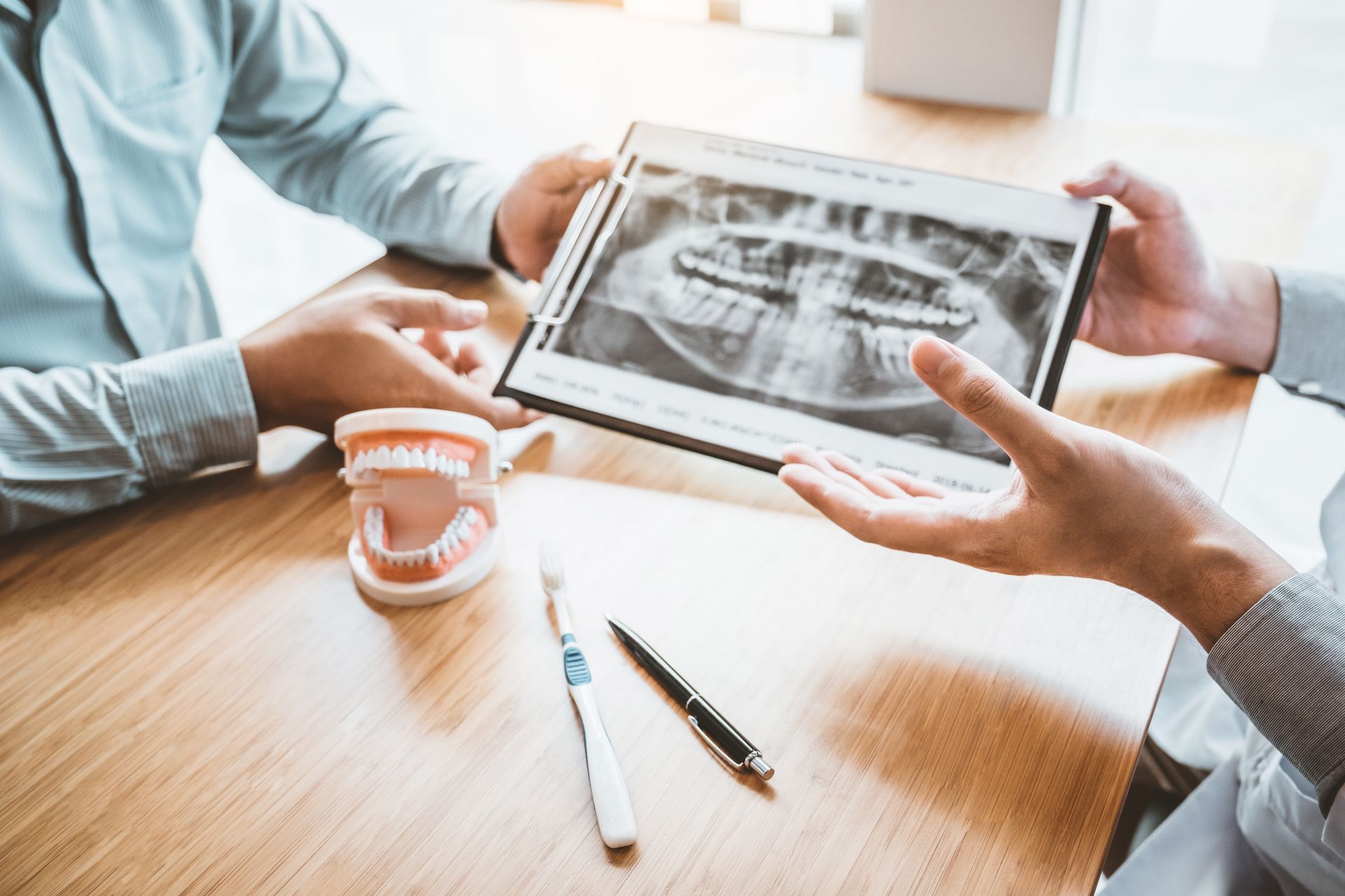 Dentist showing dental x-rays to a patient across a table with toothbrushes and dental tools