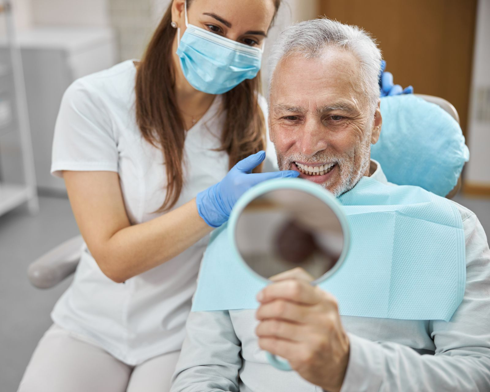 Dental hygienist wearing gloves and mask examining a smiling patient with a mirror in a clinic