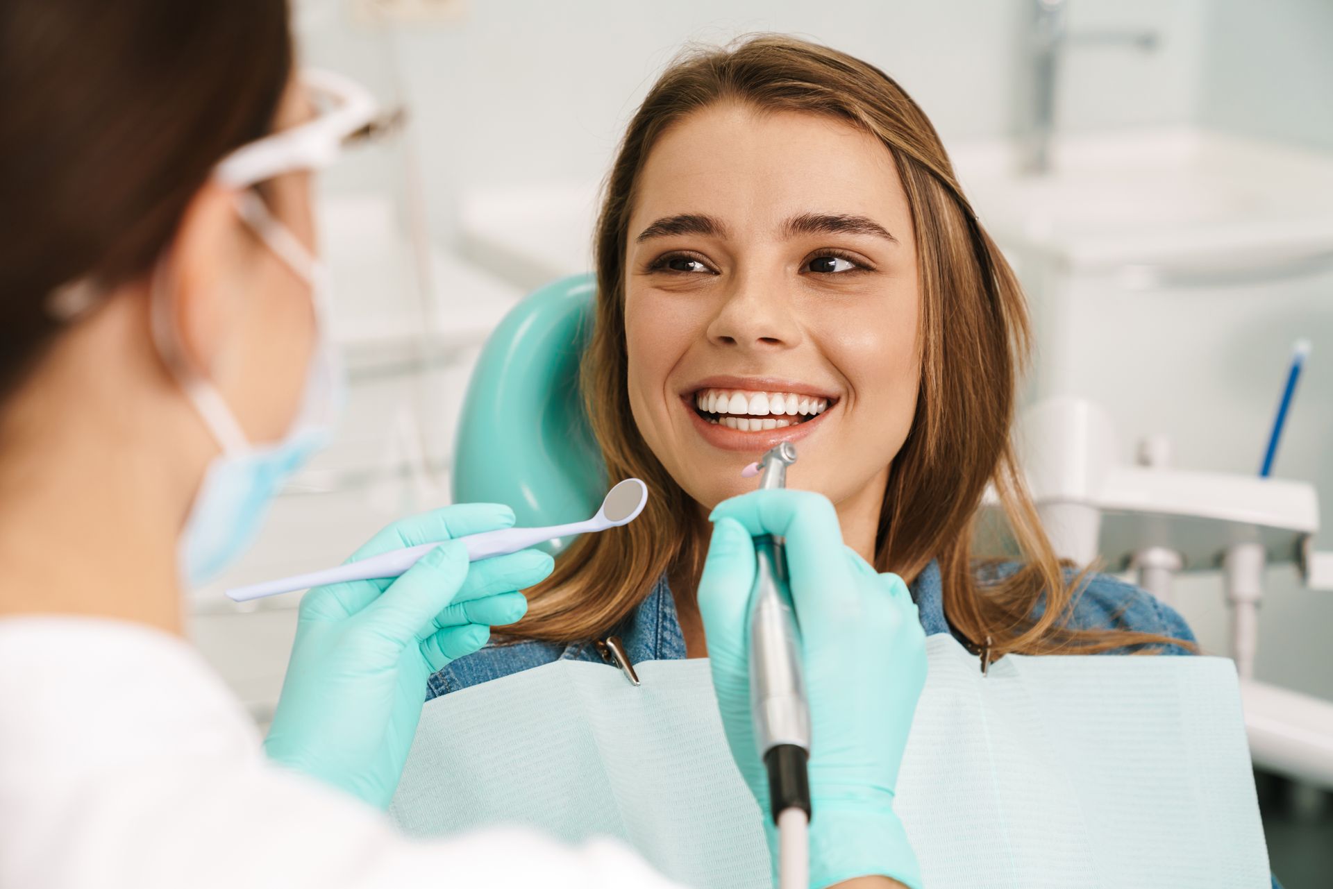 Dentist examining a smiling patient in a dental chair with tools and blue gloves
