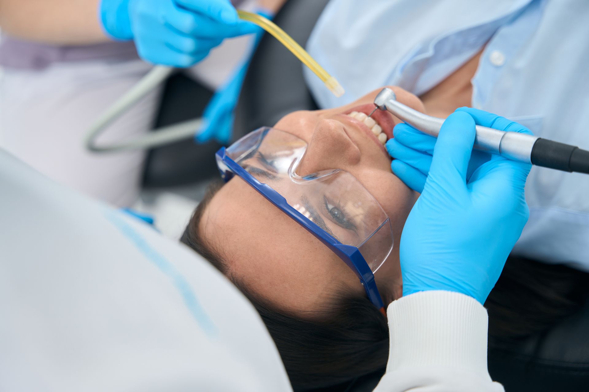 Dentist using tools to clean a patient’s teeth, with protective glasses on a dental chair