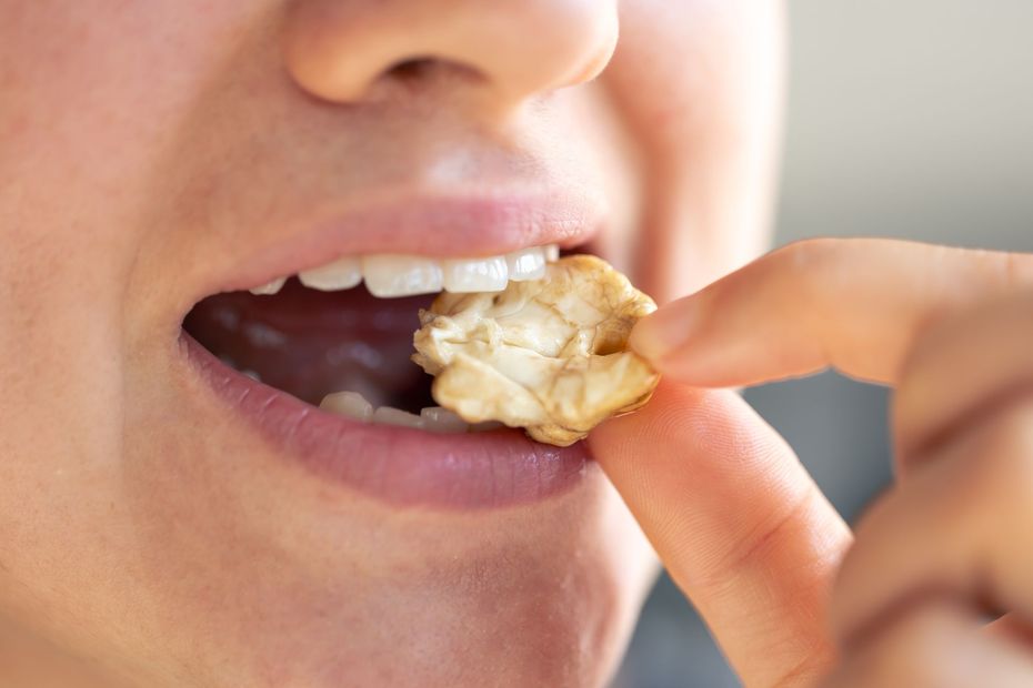 Close-up of a person biting a piece of popcorn or popcorn-flavored snack.