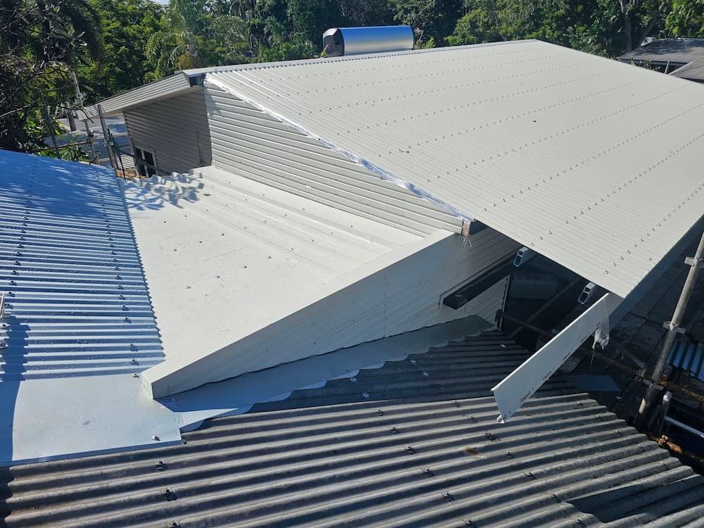 A white, slanted roof section attached to a dark corrugated roof. The setting is outdoors — KNG Roofing And Construction in Darwin, NT