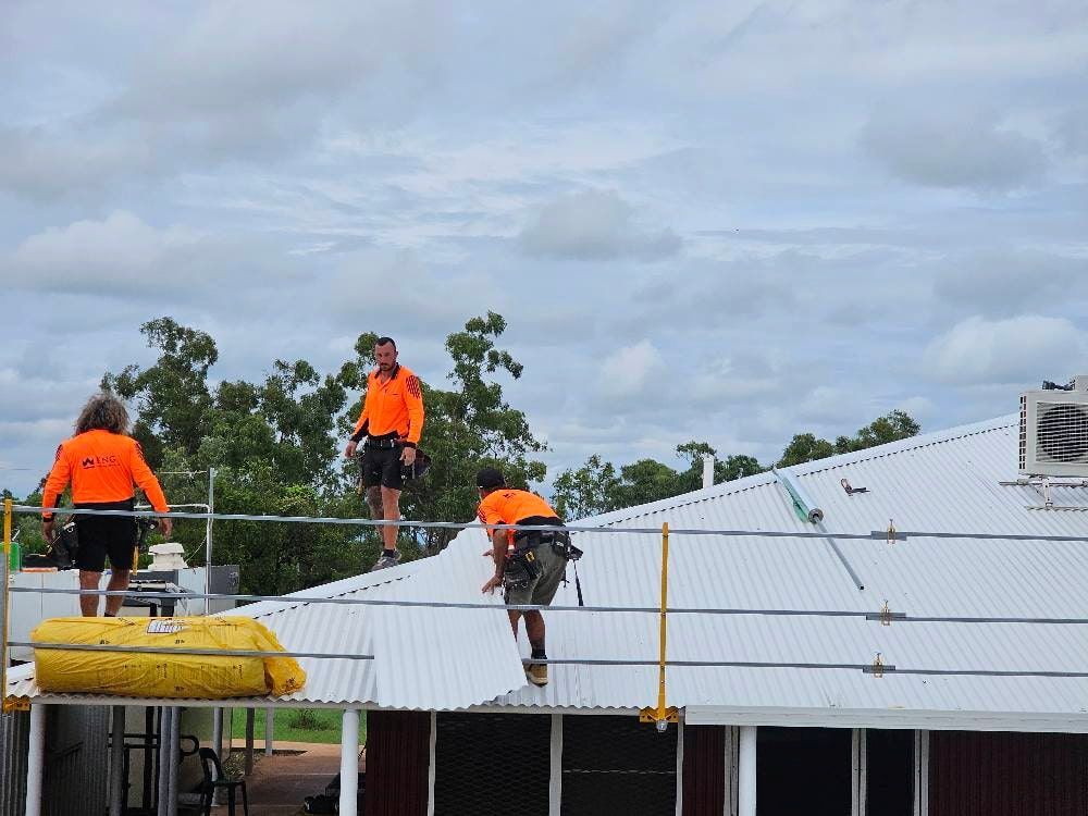 Three Workers in Orange Shirts on a Rooftop, Installing Solar Panels — KNG Roofing And Construction in Darwin, NT