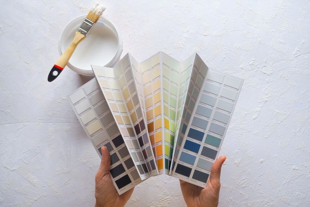 Hands Holding Open Paint Colour Swatches Next to a Paint Can and Brush — KNG Roofing And Construction in Humpty Doo, NT