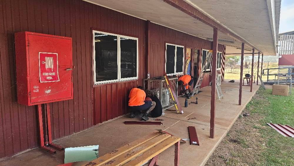 Workers in Orange Vests Repair Windows on a Red Building With a Fire Hydrant Box — KNG Roofing And Construction in Darwin, NT
