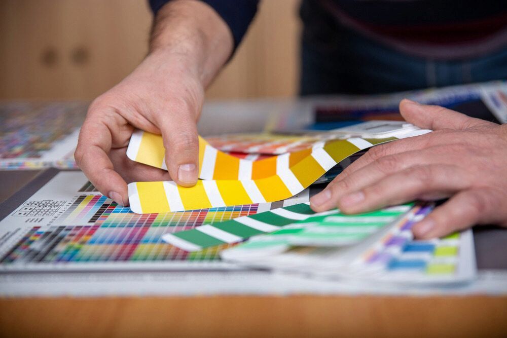 Person Comparing Yellow Colour Swatches With Printed Colour Charts — KNG Roofing And Construction in Darwin, NT