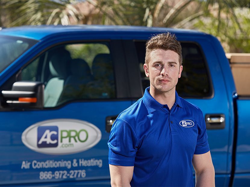 Man in blue polo standing beside blue AC Pro service truck outdoors