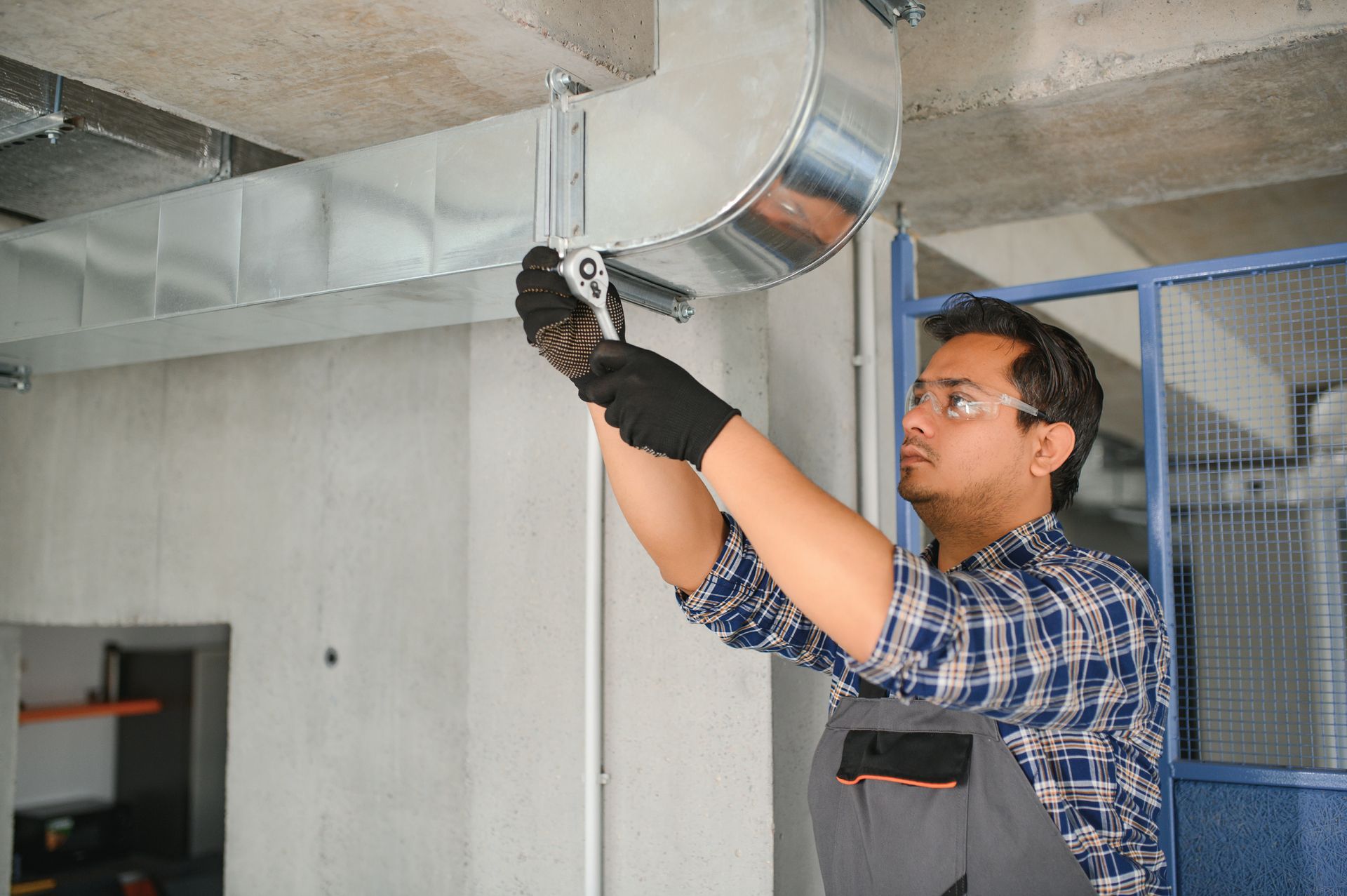 Worker installing ductwork overhead in an industrial room.