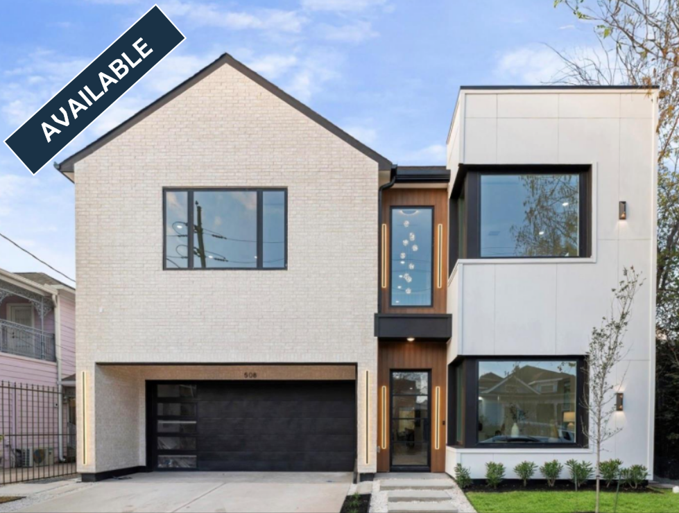 Modern white home under construction with black trim, windows, and garage door. Lush green lawn.