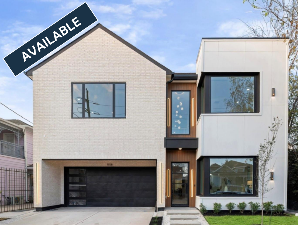 Modern white home under construction with black trim, windows, and garage door. Lush green lawn.