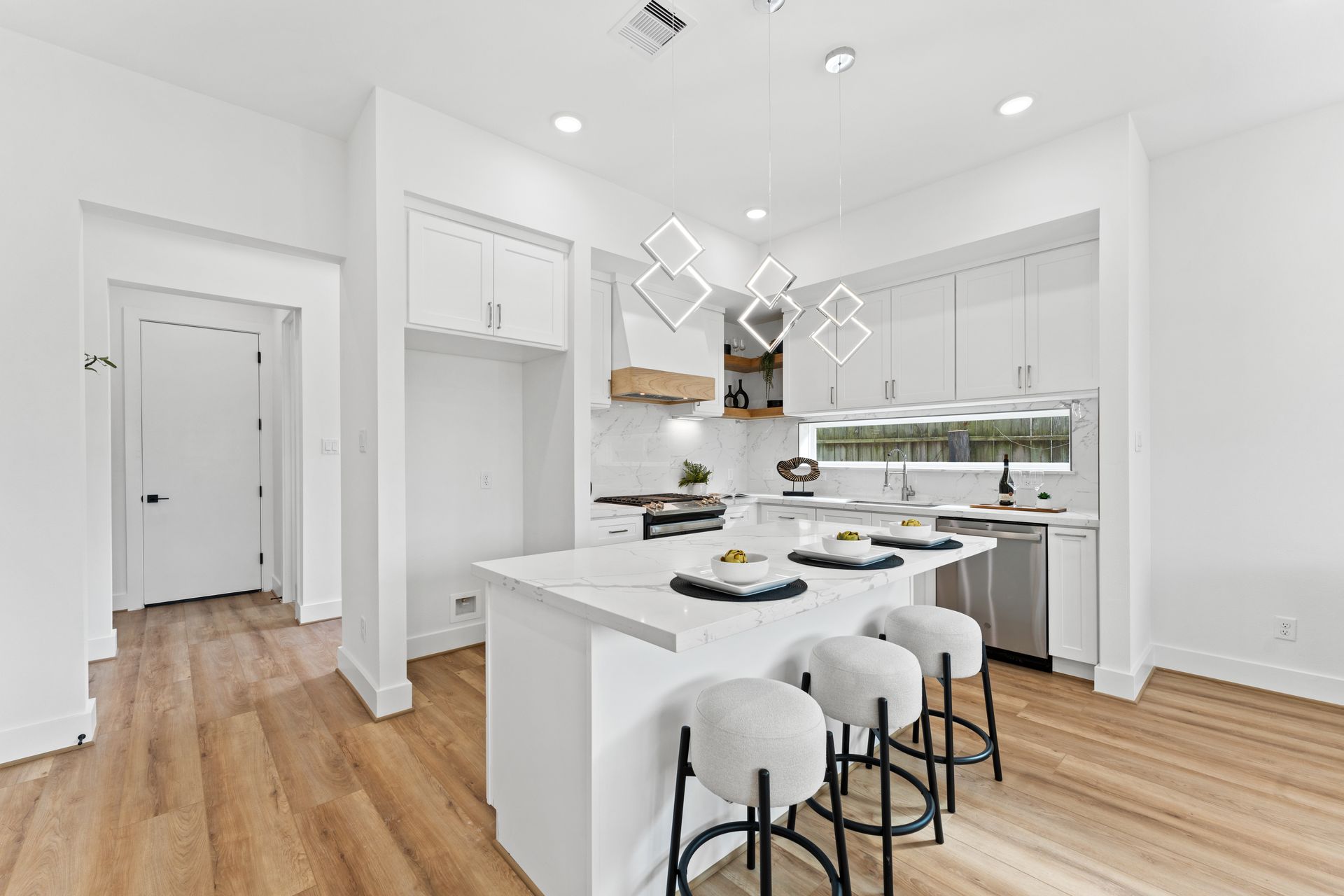 Modern white kitchen with island, light wood floors, and bar stools.