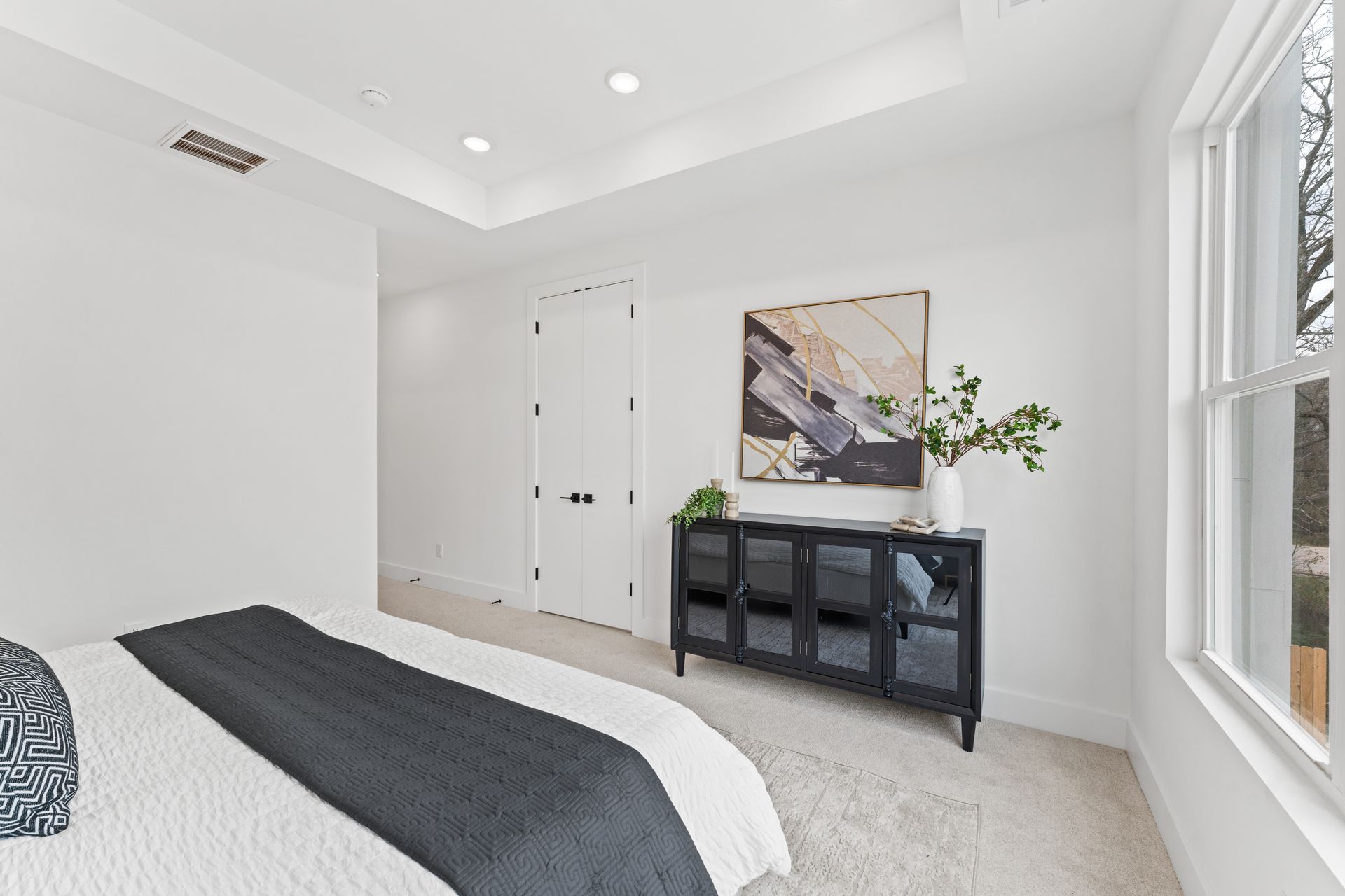 White bedroom with bed, black cabinet with art, and a window.