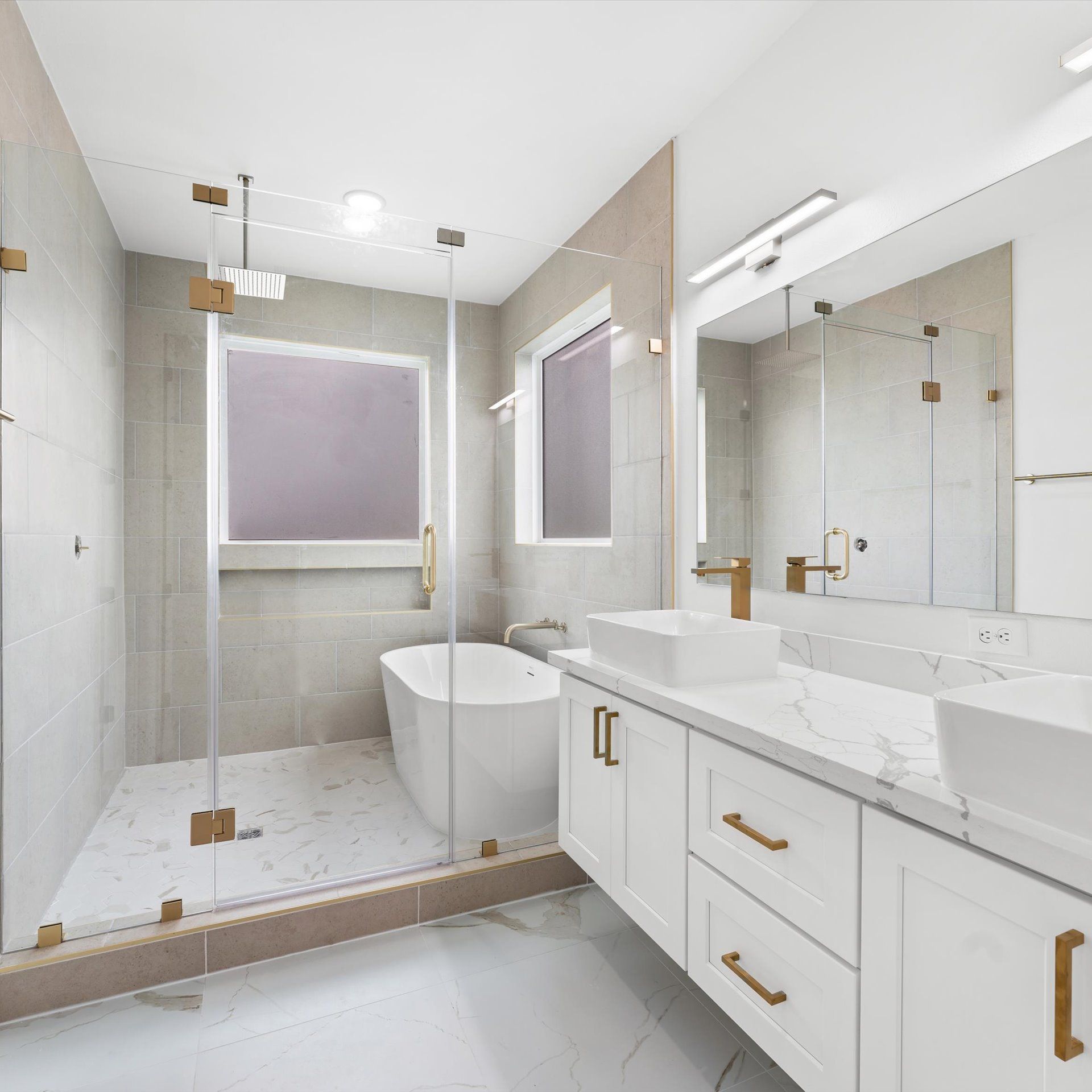Modern bathroom with white vanity, marble countertop, glass shower, and freestanding tub.