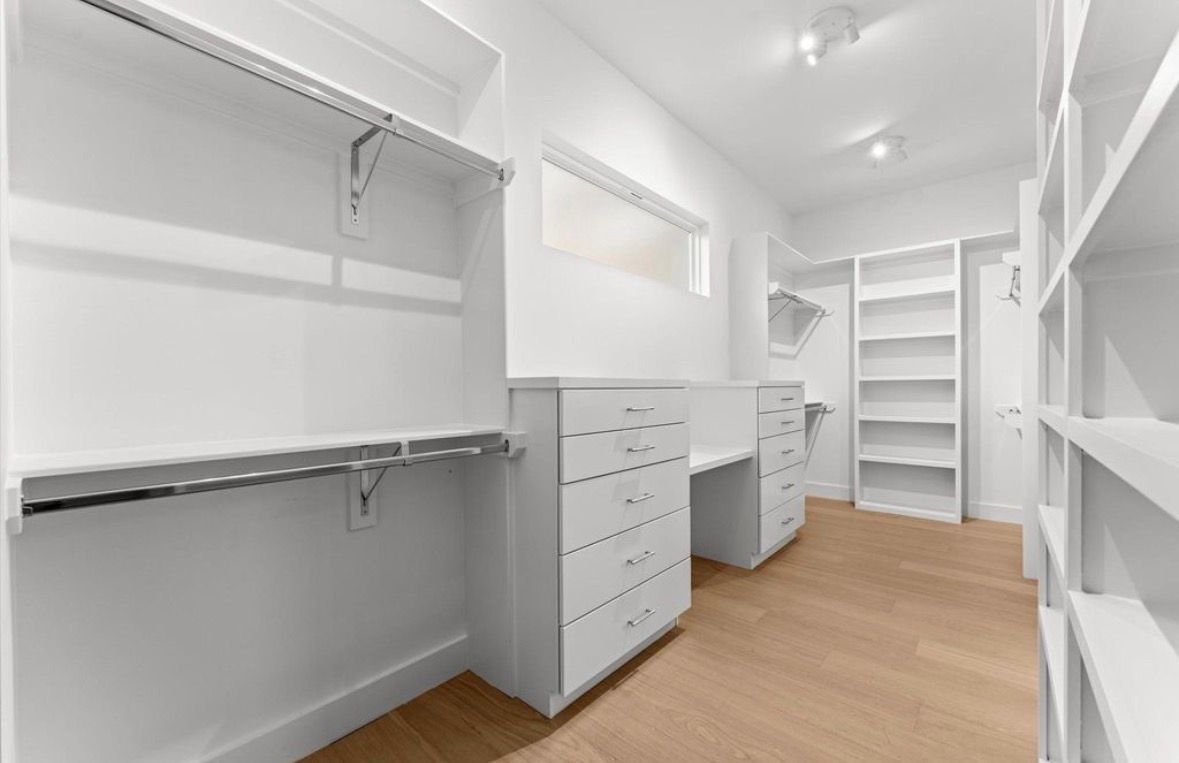 Spacious walk in closet with custom shelving drawers and wood flooring in modern Houston home