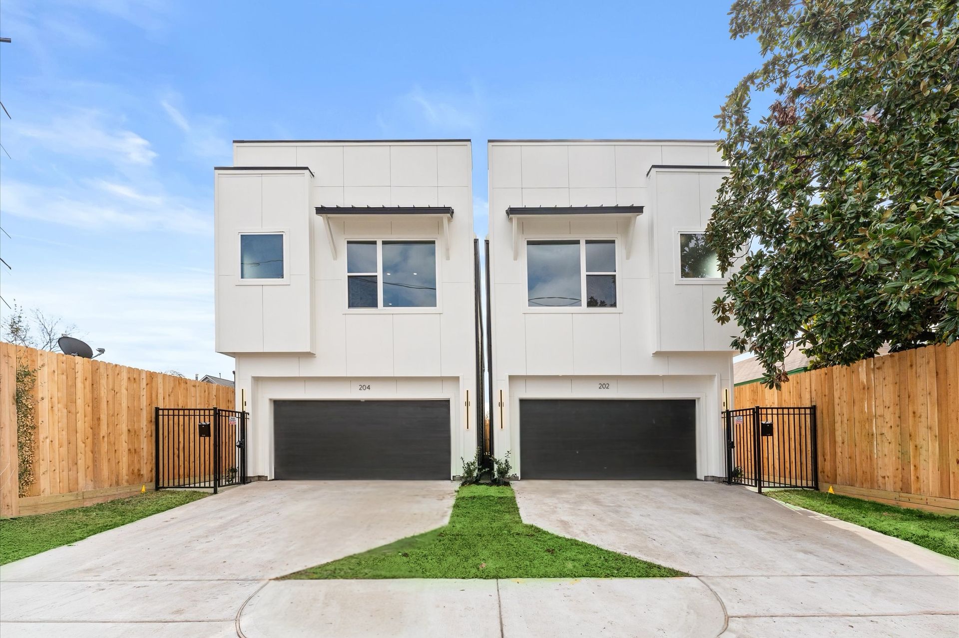 Two-story white townhomes with black garage doors, matching fences, and a small patch of grass.