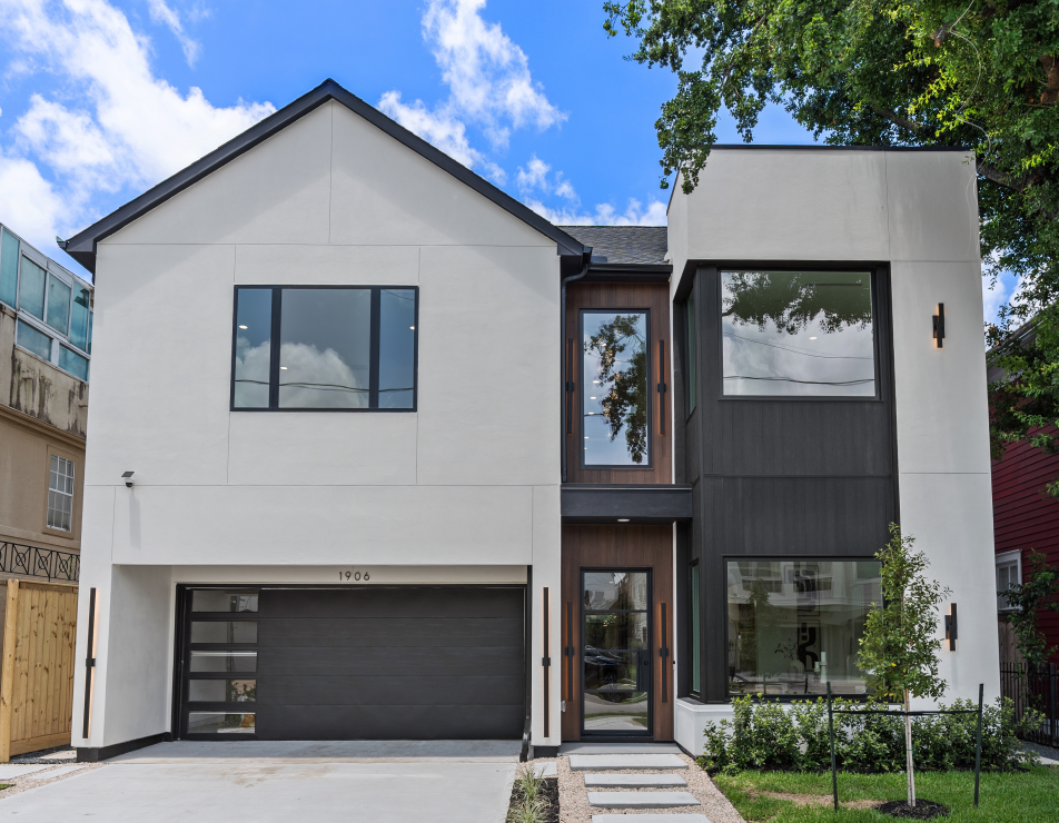 Modern white two-story house with black accents, driveway, and a blue sky.