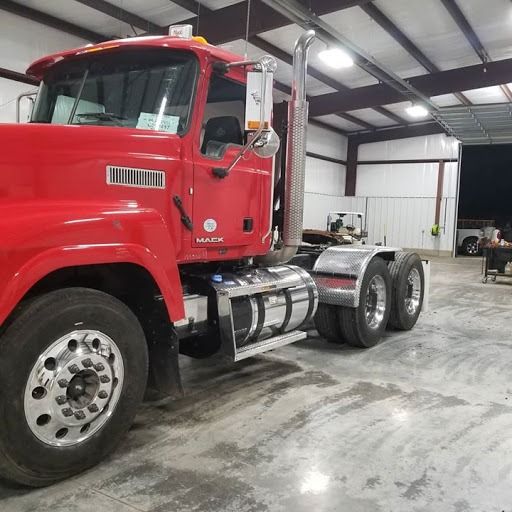 Red Mack truck parked inside a garage, next to a white trailer.