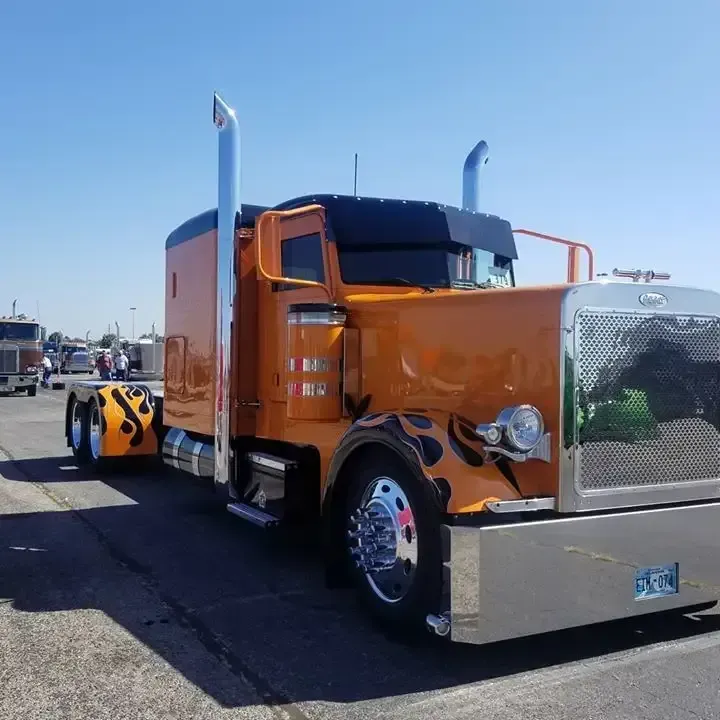 Orange and black custom semi-truck with chrome accents, flame details, and tall exhaust pipes.