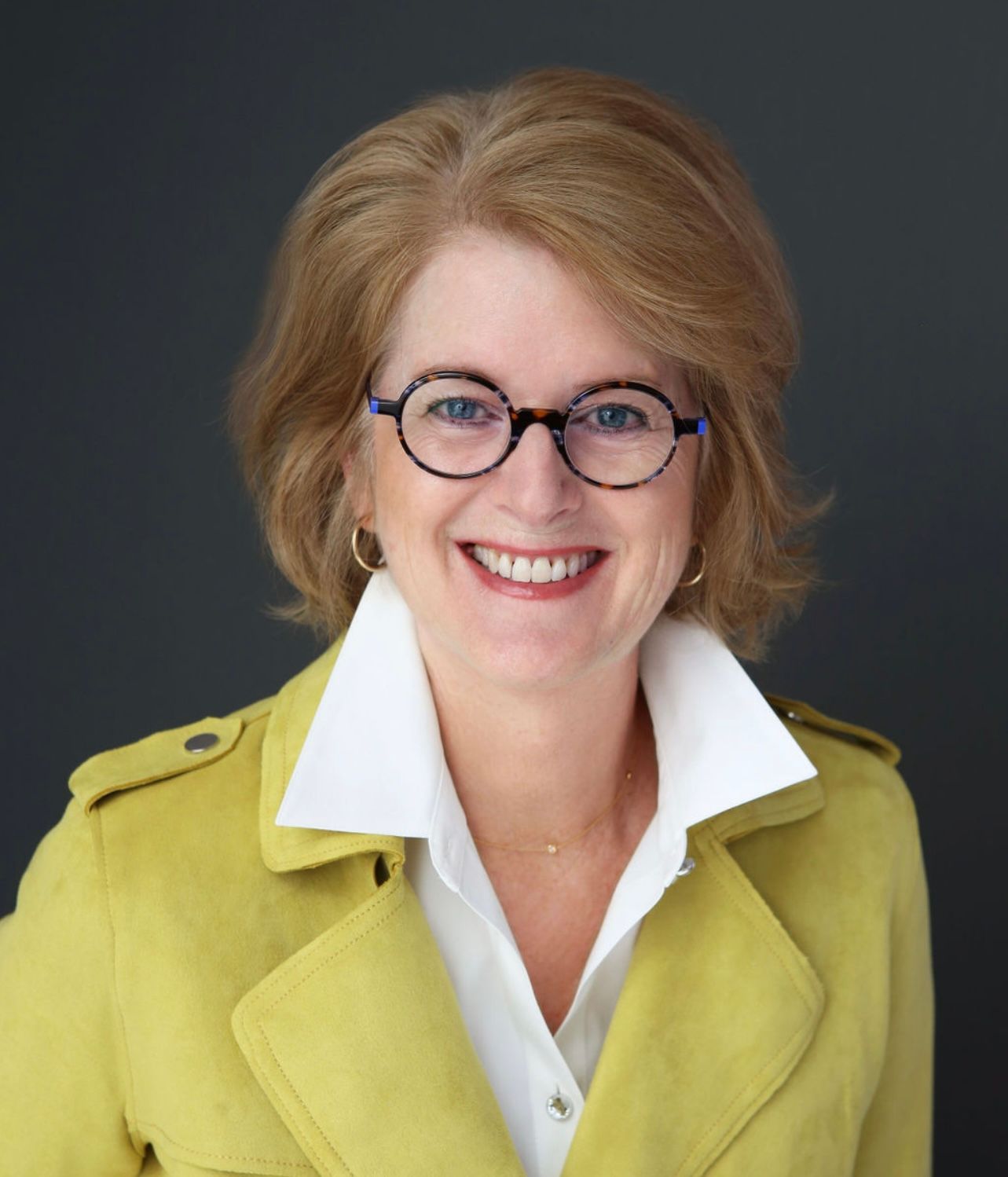 Portrait of a smiling woman in glasses and a yellow jacket against a dark background