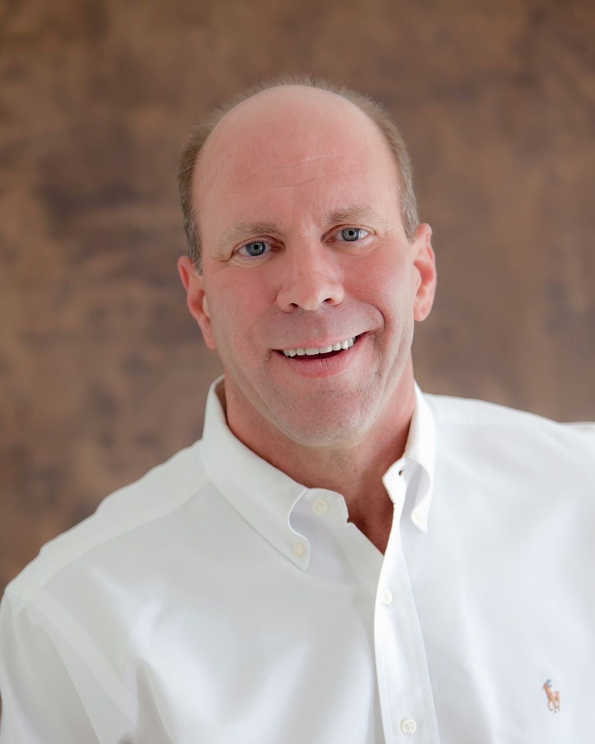 Portrait of a smiling man in a white shirt against a soft brown backdrop