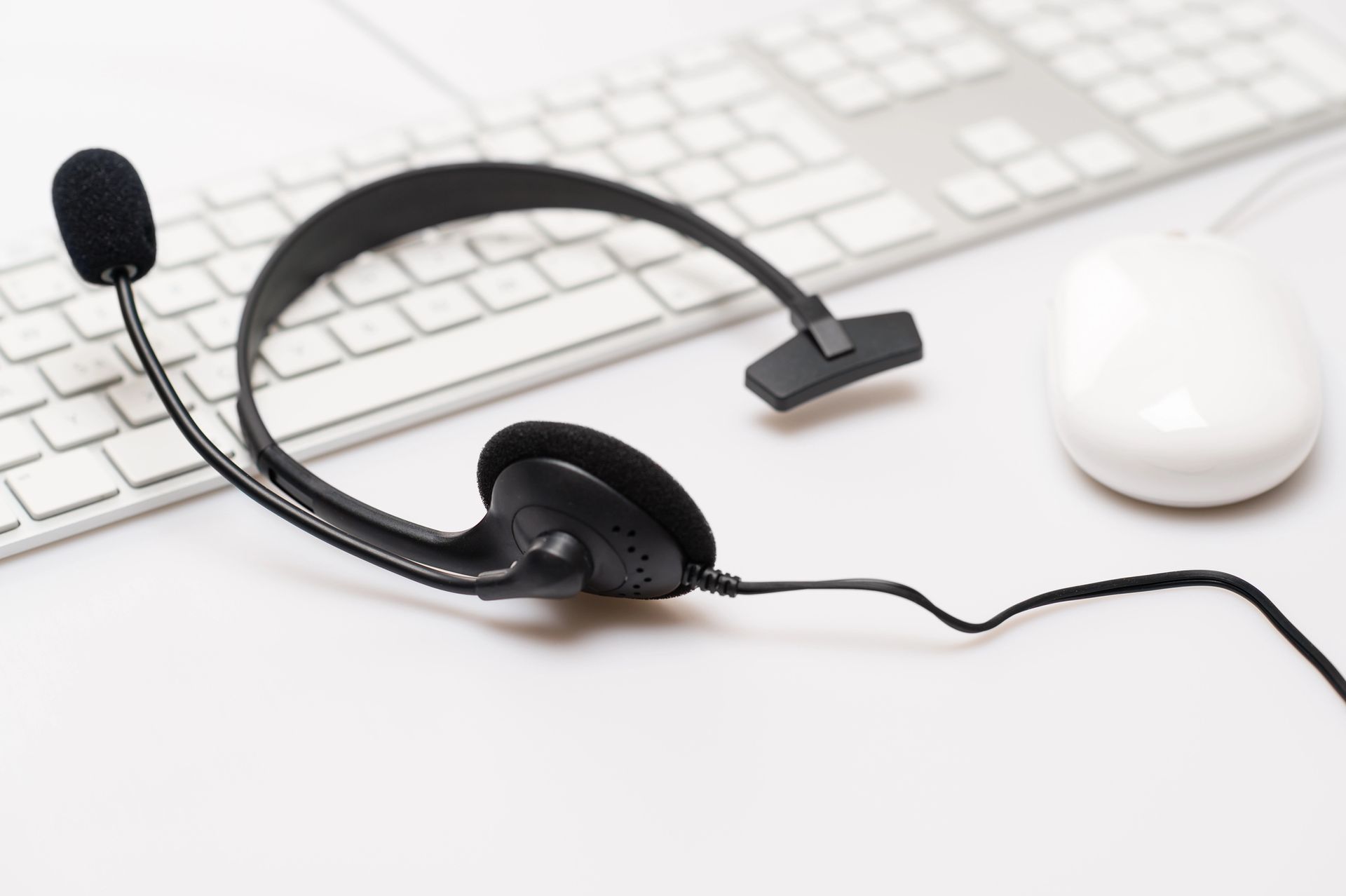 Auriculares negros con micrófono sobre un escritorio blanco junto a un teclado y un ratón.