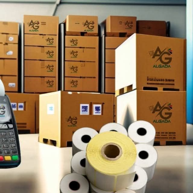 Cajas de cartón y rollos de papel apilados en un almacén, con un escáner de código de barras portátil en primer plano.