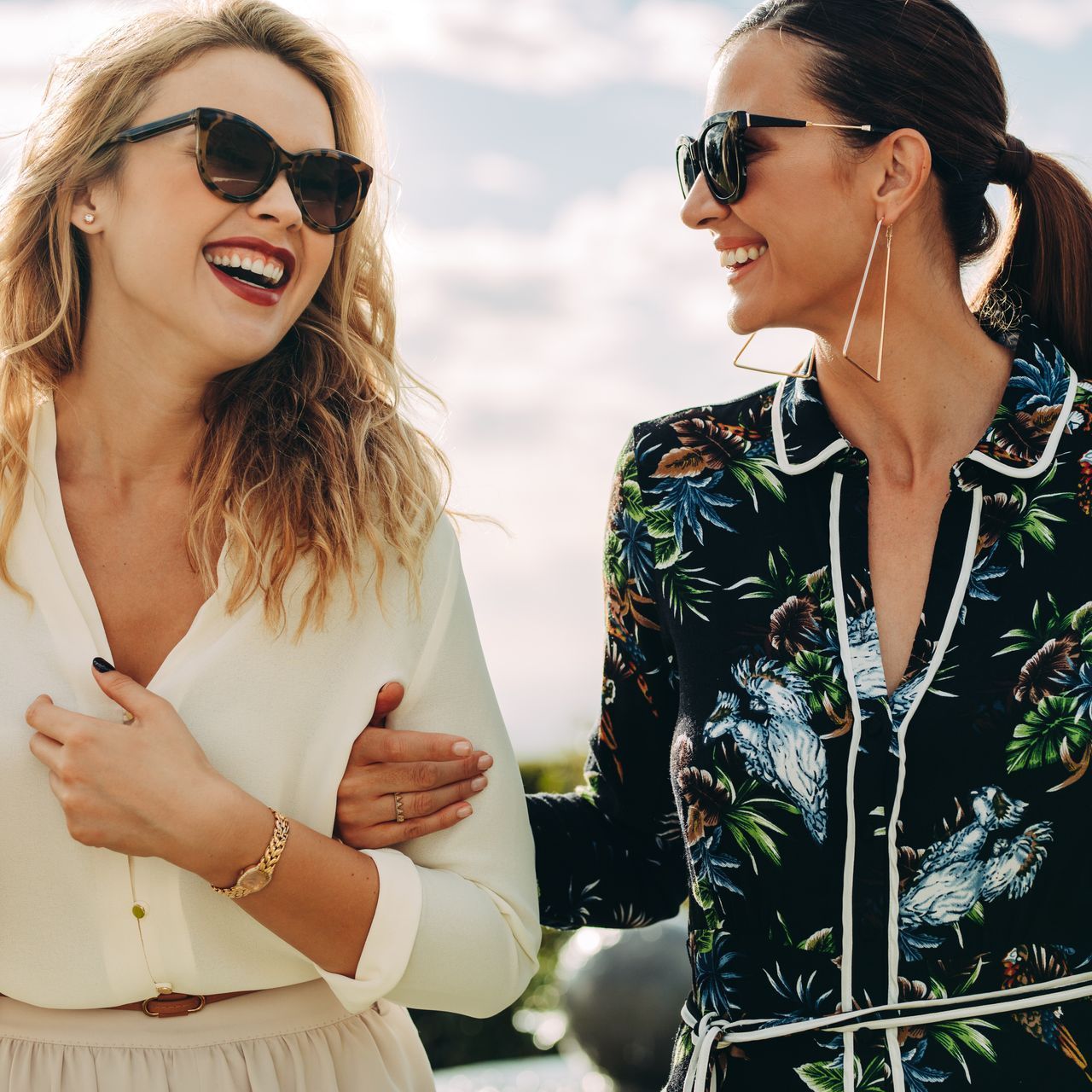 two women wearing sunglasses smiling and sharing a warm moment