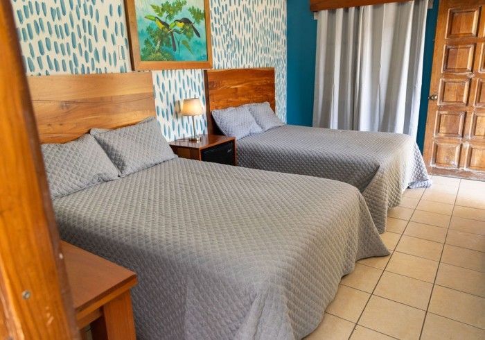 Camas individuales con colchas acolchadas de color gris, mesita de noche y obras de arte en una habitación.